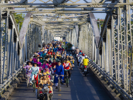 Ảnh đoàn xe đạp qua cầu Trường Tiền nổi bật trong ánh sáng sớm mai tại sự kiện "Áo dài qua phố 2025" 